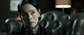 Movie still from “The Orphanage” (2007), directed by J.A. Bayona – An older woman sitting in a chair looking at the camera; Close Up shot, Over the shoulder angle