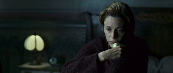 Movie still from “The Orphanage” (2007), directed by J.A. Bayona – A woman sitting on a couch holding an apple in her hand; Close Up shot, High angle