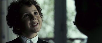 Movie still from “The Orphanage” (2007), directed by J.A. Bayona – A young boy with curly black hair wearing a white shirt and tie; Close Up shot, Low angle