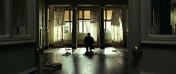 Movie still from “The Orphanage” (2007), directed by J.A. Bayona – A man sitting in front of two windows in a room; Wide shot, Low angle