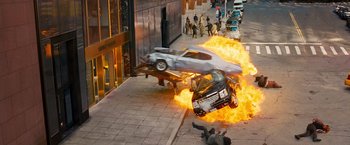 Movie still from “The Other Guys” (2010), directed by Adam McKay – A car on fire in a street with a person laying on the ground; Extreme Wide shot, High angle