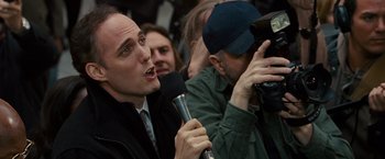 Movie still from “The Other Guys” (2010), directed by Adam McKay – A man holding a microphone while standing in front of a group of people; Close Up shot, High angle
