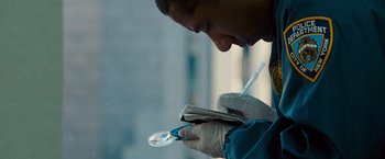 Movie still from “The Other Guys” (2010), directed by Adam McKay – A man writing on a piece of paper while holding a magnifying glass; Extreme Close Up shot, Over the shoulder angle