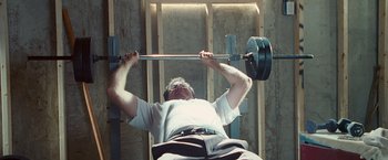 Movie still from “The Other Guys” (2010), directed by Adam McKay – A man is lifting a barbell in a gym; Medium shot, Low angle