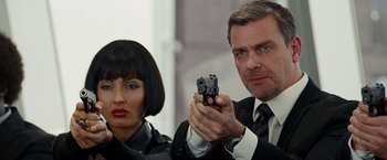 Movie still from “The Other Guys” (2010), directed by Adam McKay – A man and a woman holding a gun in front of a building; Close Up shot, Over the shoulder angle