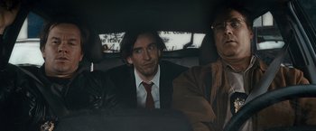 Movie still from “The Other Guys” (2010), directed by Adam McKay – A man sitting in the back seat of a car with two other men; Medium shot, Over the shoulder angle