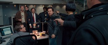 Movie still from “The Other Guys” (2010), directed by Adam McKay – A group of people standing around a table; Medium shot, Over the shoulder angle