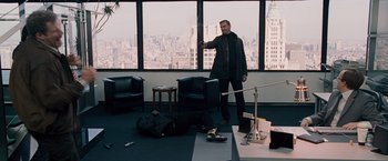 Movie still from “The Other Guys” (2010), directed by Adam McKay – A man standing in front of a large window with luggage; Wide shot, High angle