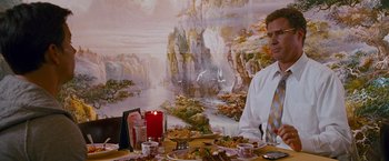 Movie still from “The Other Guys” (2010), directed by Adam McKay – A man sitting at a dinner table in front of a painting; Medium shot, Over the shoulder angle