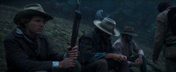 Movie still from “The Outlaw Josey Wales” (1976), directed by Clint Eastwood – A man sitting on the ground holding a rifle; Medium shot, Low angle