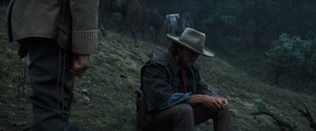 Movie still from “The Outlaw Josey Wales” (1976), directed by Clint Eastwood – A man sitting on the ground in front of a herd of cattle; Medium shot, Low angle