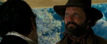 Movie still from “The Outlaw Josey Wales” (1976), directed by Clint Eastwood – A man with a beard wearing a hat looking at another man with a beard wearing a hat; Close Up shot, Over the shoulder angle