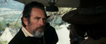 Movie still from “The Outlaw Josey Wales” (1976), directed by Clint Eastwood – A man with long hair and a goatee looking at another man with long hair; Close Up shot, Over the shoulder angle