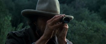 Movie still from “The Outlaw Josey Wales” (1976), directed by Clint Eastwood – A man in a hat is looking through a telescope; Close Up shot, Over the shoulder angle