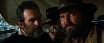 Movie still from “The Outlaw Josey Wales” (1976), directed by Clint Eastwood – Two men with a beard and a hat are looking at the camera; Close Up shot, Over the shoulder angle