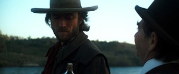 Movie still from “The Outlaw Josey Wales” (1976), directed by Clint Eastwood – A man with a hat and a beard holding a bottle; Close Up shot, Over the shoulder angle