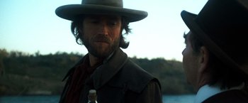 Movie still from “The Outlaw Josey Wales” (1976), directed by Clint Eastwood – A person wearing a hat and holding a bottle; Close Up shot, Over the shoulder angle