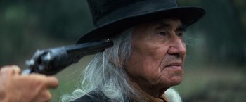 Movie still from “The Outlaw Josey Wales” (1976), directed by Clint Eastwood – An old man with long white hair wearing a black hat; Close Up shot, Over the shoulder angle