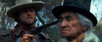Movie still from “The Outlaw Josey Wales” (1976), directed by Clint Eastwood – A man holding a gun in front of an older man; Close Up shot, Over the shoulder angle