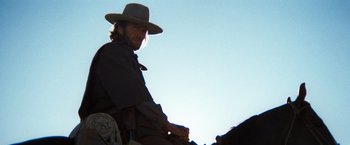 Movie still from “The Outlaw Josey Wales” (1976), directed by Clint Eastwood – A man with a cowboy hat sitting on top of a horse; Medium shot, Low angle