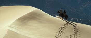 Movie still from “The Outlaw Josey Wales” (1976), directed by Clint Eastwood – Two people on horseback riding up a sand dune; Extreme Wide shot, High angle