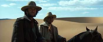 Movie still from “The Outlaw Josey Wales” (1976), directed by Clint Eastwood – A man and a woman wearing hats standing next to each other in the desert; Wide shot, Low angle