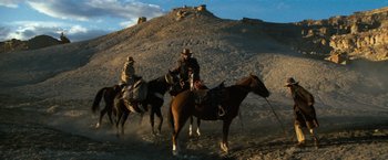 Movie still from “The Outlaw Josey Wales” (1976), directed by Clint Eastwood – A group of people riding horses on a dirt road; Wide shot, Low angle