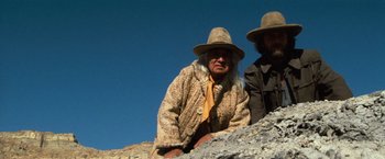Movie still from “The Outlaw Josey Wales” (1976), directed by Clint Eastwood – Two men in hats and a fur coat on top of a hill; Medium shot, Low angle