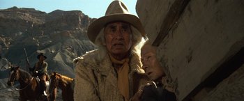 Movie still from “The Outlaw Josey Wales” (1976), directed by Clint Eastwood – An old man and a woman in a hat and a fur coat; Medium shot, Low angle