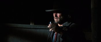 Movie still from “The Outlaw Josey Wales” (1976), directed by Clint Eastwood – A man in a hat holding a cell phone in a dark room; Close Up shot, Over the shoulder angle