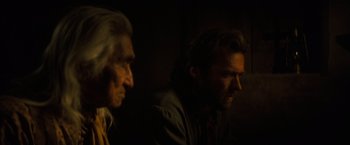 Movie still from “The Outlaw Josey Wales” (1976), directed by Clint Eastwood – A man and an old man sitting next to each other in a dark room; Close Up shot, Over the shoulder angle