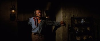 Movie still from “The Outlaw Josey Wales” (1976), directed by Clint Eastwood – A man in a blue shirt and brown pants holding a knife; Medium shot, Low angle
