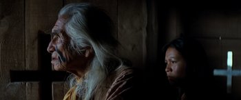 Movie still from “The Outlaw Josey Wales” (1976), directed by Clint Eastwood – Two people standing in a dark room , one of which has long white hair; Close Up shot, Over the shoulder angle