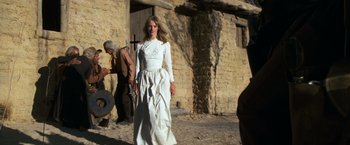 Movie still from “The Outlaw Josey Wales” (1976), directed by Clint Eastwood – A woman in a white dress standing in front of a building; Medium shot, Low angle