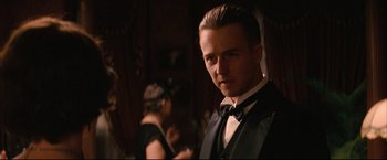 Movie still from “The Painted Veil” (2006), directed by John Curran – A man in a suit and bow - tie standing in front of other people; Close Up shot, Over the shoulder angle