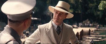 Movie still from “The Painted Veil” (2006), directed by John Curran – A man in a suit and hat standing in front of trees; Close Up shot, Over the shoulder angle
