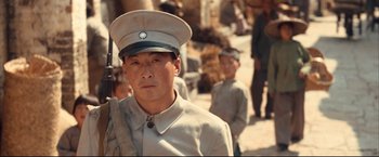 Movie still from “The Painted Veil” (2006), directed by John Curran – An asian man in a military uniform is holding a rifle; Close Up shot, Over the shoulder angle
