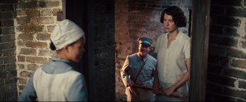 Movie still from “The Painted Veil” (2006), directed by John Curran – A group of people standing next to each other in front of a brick wall; Medium shot, Over the shoulder angle