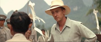 Movie still from “The Painted Veil” (2006), directed by John Curran – A man wearing a straw hat standing in front of a group of people; Close Up shot, Over the shoulder angle