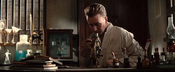 Movie still from “The Painted Veil” (2006), directed by John Curran – A man looking through a microscope in a room; Close Up shot, High angle