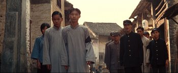 Movie still from “The Painted Veil” (2006), directed by John Curran – A group of young men standing next to each other on a street; Medium shot, Low angle