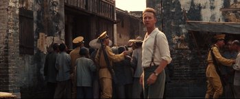 Movie still from “The Painted Veil” (2006), directed by John Curran – A man in a white shirt is standing in front of a group of people; Medium shot, Over the shoulder angle