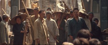 Movie still from “The Painted Veil” (2006), directed by John Curran – A group of people walking down a street holding sticks; Medium shot, High angle