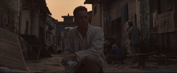 Movie still from “The Painted Veil” (2006), directed by John Curran – A man sitting on the ground in the middle of a street; Medium shot, Low angle