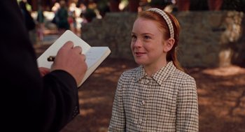 Movie still from “The Parent Trap” (1998), directed by Nancy Meyers – A young girl smiles as a man writes on a piece of paper in front of her; Medium shot, Over the shoulder angle