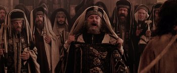 Movie still from “The Passion of the Christ” (2004), directed by Mel Gibson – A man with a long beard is holding a robe over his head; Medium shot, Low angle