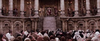 Movie still from “The Passion of the Christ” (2004), directed by Mel Gibson – A group of people sitting on steps in front of a building; Extreme Wide shot, High angle