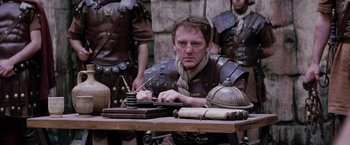 Movie still from “The Passion of the Christ” (2004), directed by Mel Gibson – A man in a roman costume writing on a table; Medium shot, Low angle