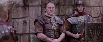 Movie still from “The Passion of the Christ” (2004), directed by Mel Gibson – A man in a roman soldier's outfit is standing in front of a stone wall; Medium shot, Low angle