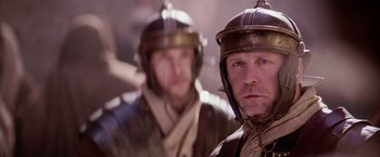 Movie still from “The Passion of the Christ” (2004), directed by Mel Gibson – Two men in roman helmets are standing together; Close Up shot, Over the shoulder angle